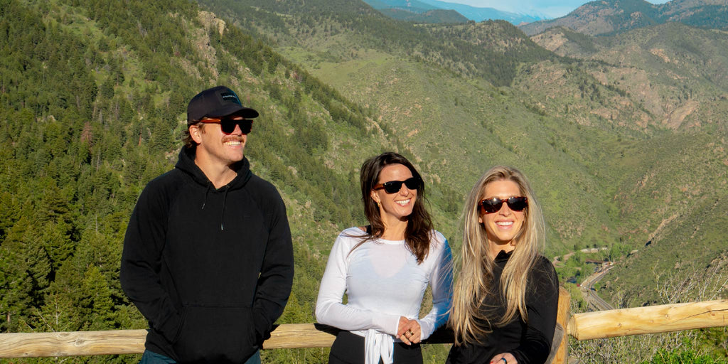 Three people standing together wearing Optic Nerve sunglasses with a scenic mountain background