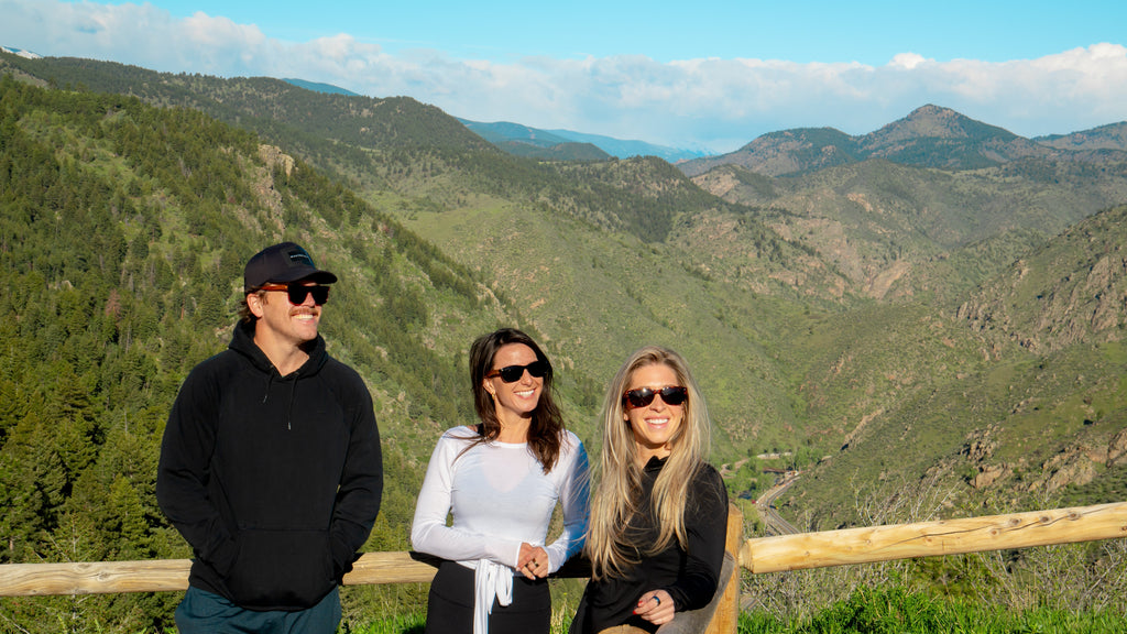 Three people standing on a wooden platform with a scenic mountain view in the background