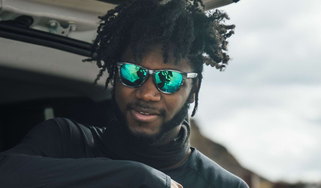 Man wearing Optic Nerve Fairplay sunglasses with a gray frame, smoke lenses, and a green mirror in the trunk of a car