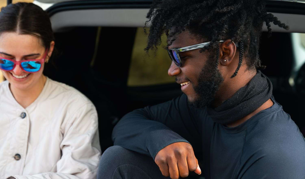 Man wearing Optic Nerve Fairplay sunglasses with a gray frame, smoke lenses, and a green mirror, sitting in a car trunk