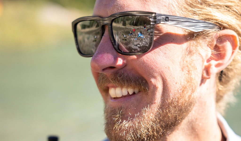 Close-up of a person wearing Optic Nerve Mashup sunglasses with a gray frame, smoke lenses, and silver mirror with a blurred background