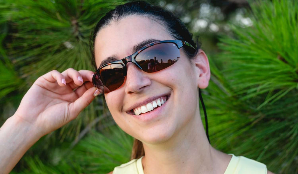 Woman wearing Optic Nerve Alpine sunglasses with tortoise frame and brown lenses in from of natural background
