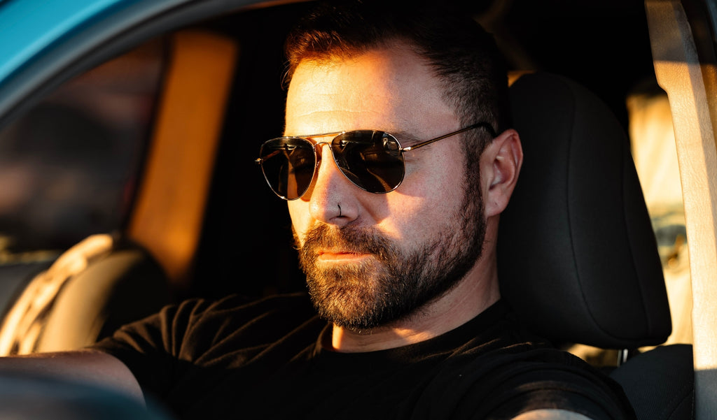 Man wearing Optic Nerve Estrada sunglasses with a silver frame and smoke lenses in the drivers seat of a car