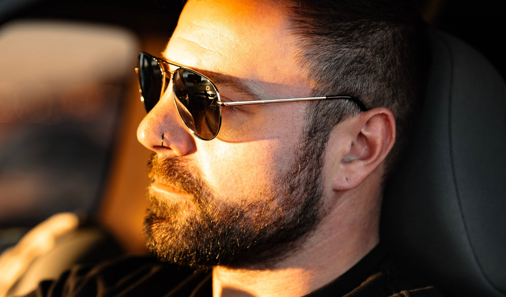 Man wearing Optic Nerve Estrada sunglasses with a silver frame and smoke lenses in the drivers seat of a car