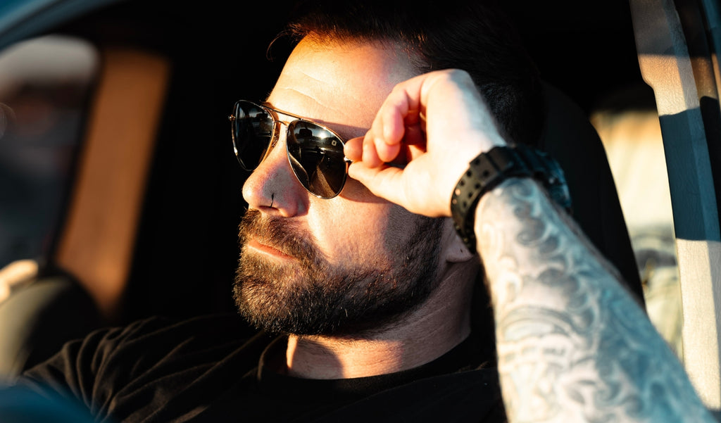 Man wearing Optic Nerve Estrada sunglasses with a silver frame and smoke lenses in the drivers seat of a car