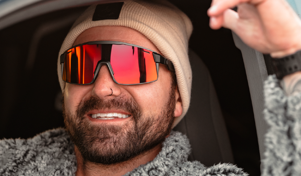 Person wearing a beanie and Optic Nerve FixieMAX sunglasses with a black frame, smoke lens, and a red mirror, inside a vehicle