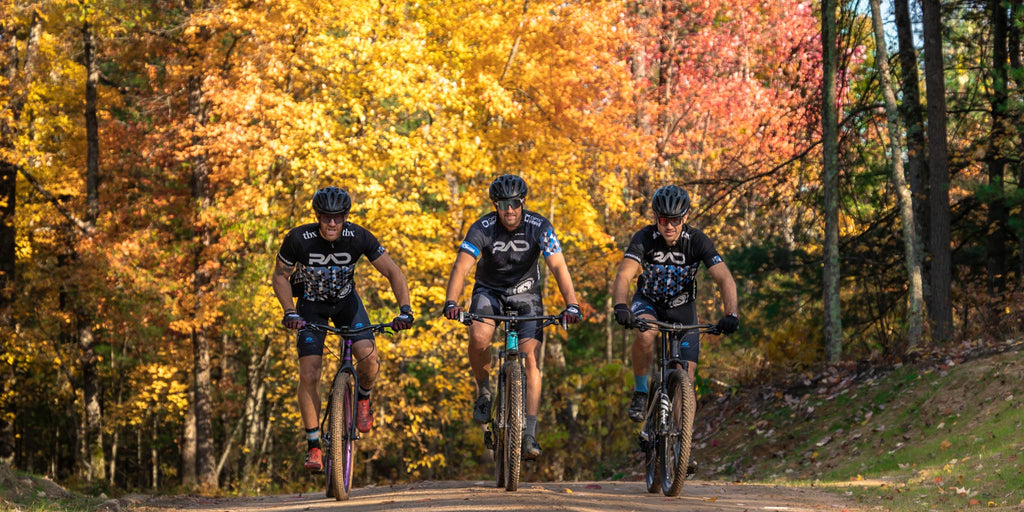 Three cyclists riding on a trail wearing Optic Nerve Sunglasses with autumn foliage