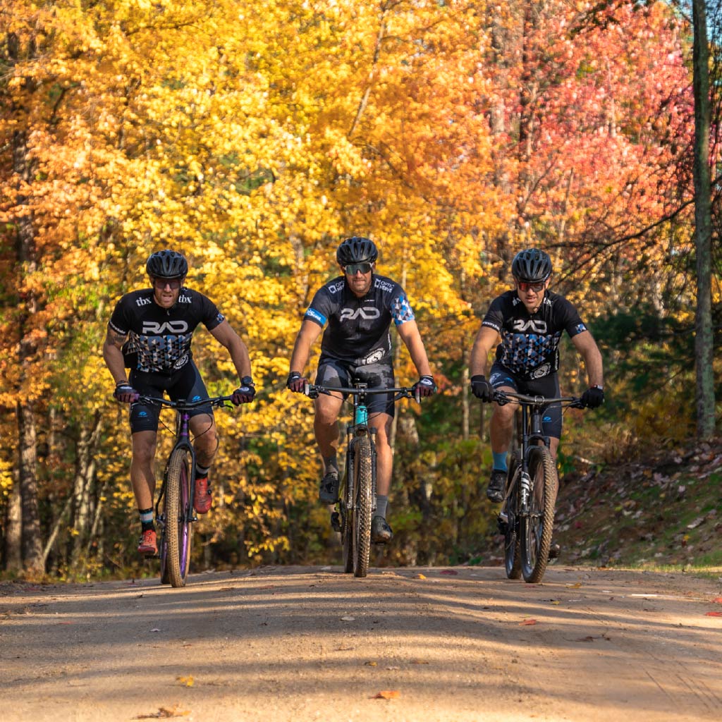 Three cyclists riding on a trail wearing Optic Nerve Sunglasses with autumn foliage