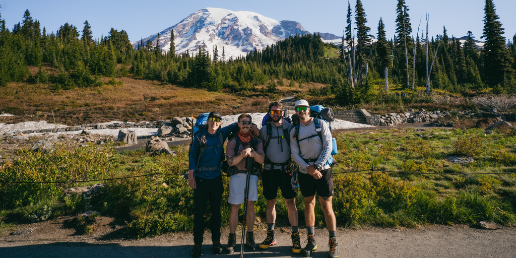 Four hikers with backpacks and Optic Nerve sunglasses standing in a forested area.