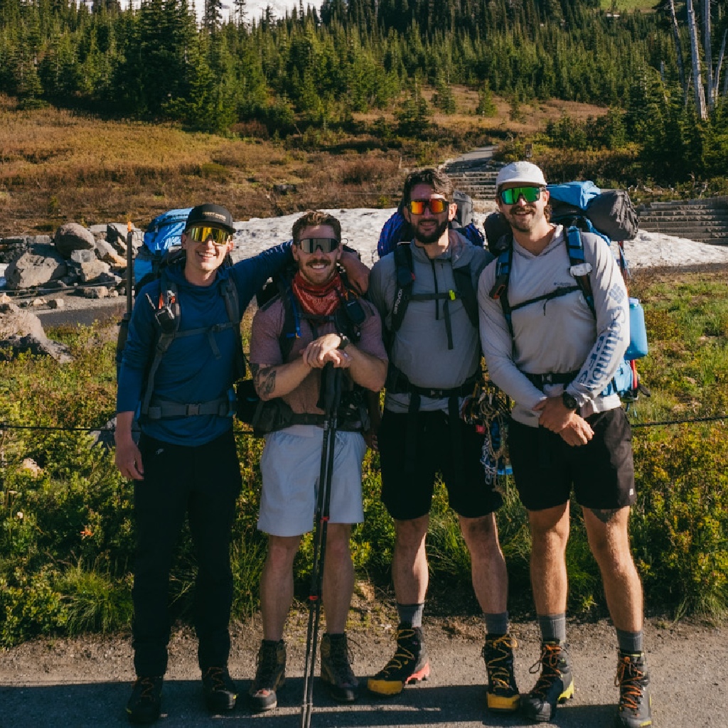 Four hikers with backpacks and Optic Nerve sunglasses standing in a forested area.