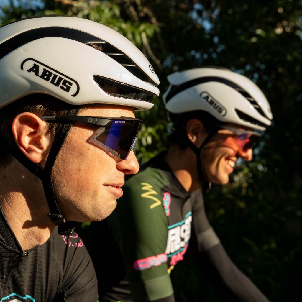 Two cyclists wearing ABUS helmets and Optic Nerve FixieAIR sunglasses with a blurred natural background