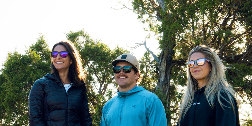 Three people standing outdoors wearing Optic Nerve sunglasses with trees in the background