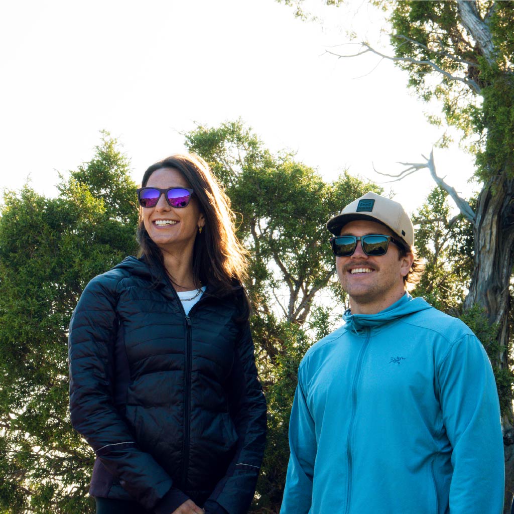 Two people standing outdoors wearing Optic Nerve sunglasses with trees in the background