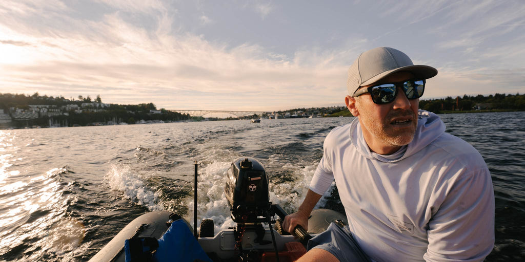 Man on a boat wearing Optic Nerve Zaldaingerous Rumble sunglasses with a black frame, amber lenses, and blue mirror, and a cap, with water and sky in the background