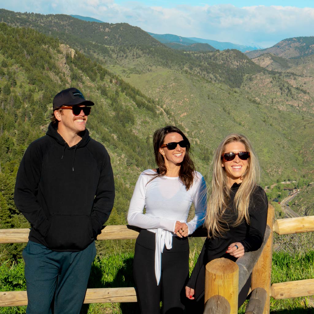 Three people standing together wearing Optic Nerve sunglasses with a scenic mountain background