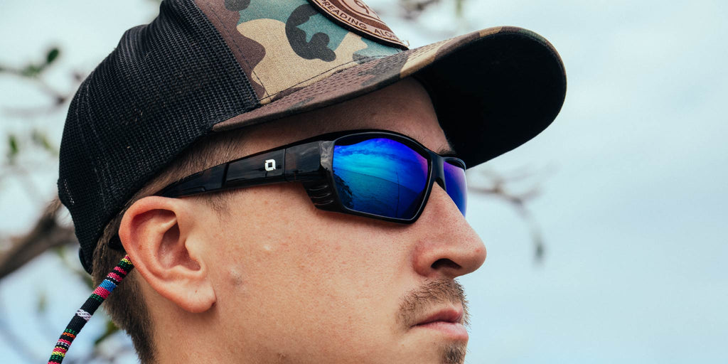 Person wearing a camouflage baseball cap and Optic Nerve Yampa sunglasses with a tortoise frame, brown lenses, and a green mirror, with a blurred natural background