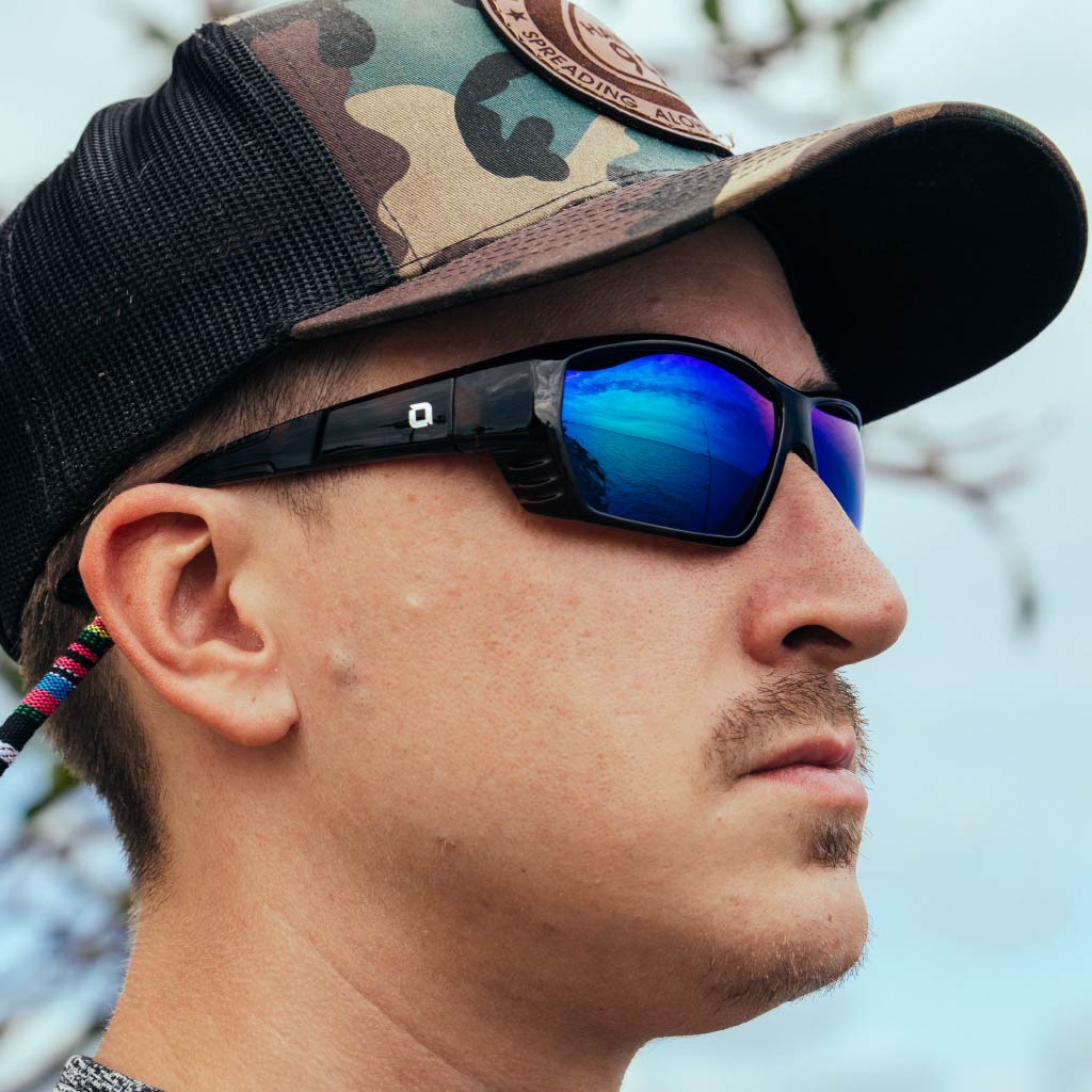 Person wearing a camouflage baseball cap and Optic Nerve Yampa sunglasses with a tortoise frame, brown lenses, and a green mirror, with a blurred natural background