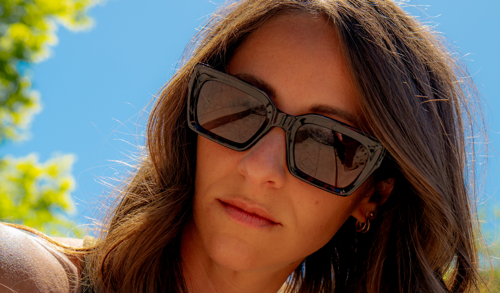 Woman wearing Optic Nerve Afterglow  sunglasses with a tortoise frame and brown lenses, with a clear blue sky and greenery in the background
