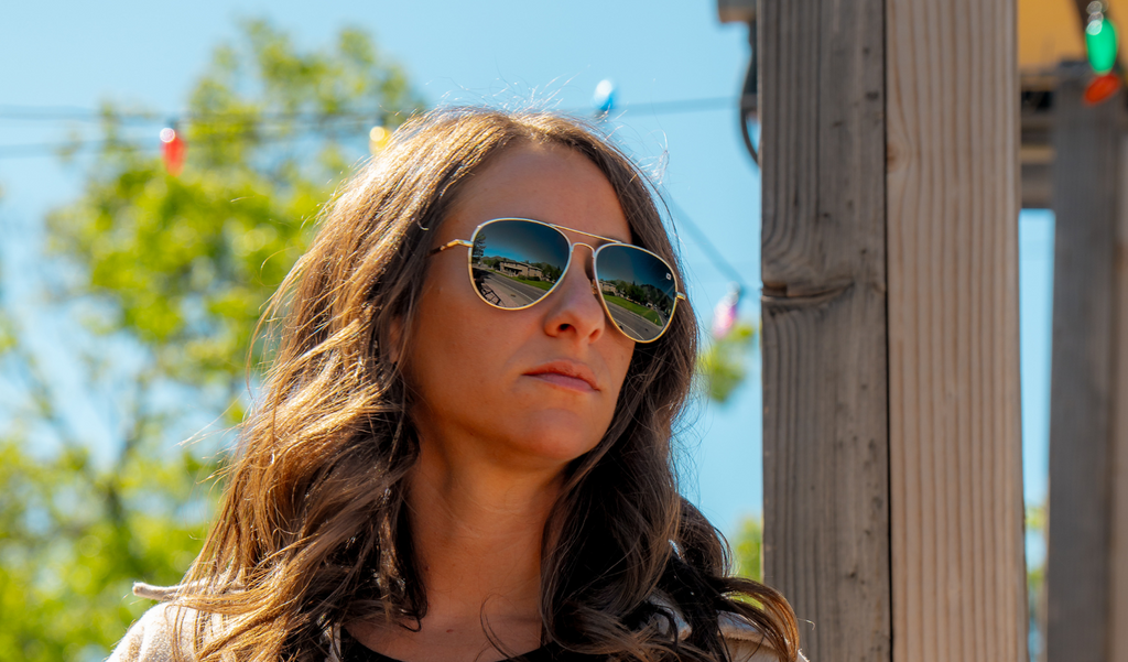 Woman wearing Optic Nerve Estrada sunglasses witha  gold frame and smoke lenses, with a blurred background