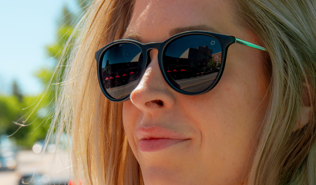 Person wearing Optic Nerve Pizmo sunglasses with a black frame and smoke lenses with a blurred outdoor background