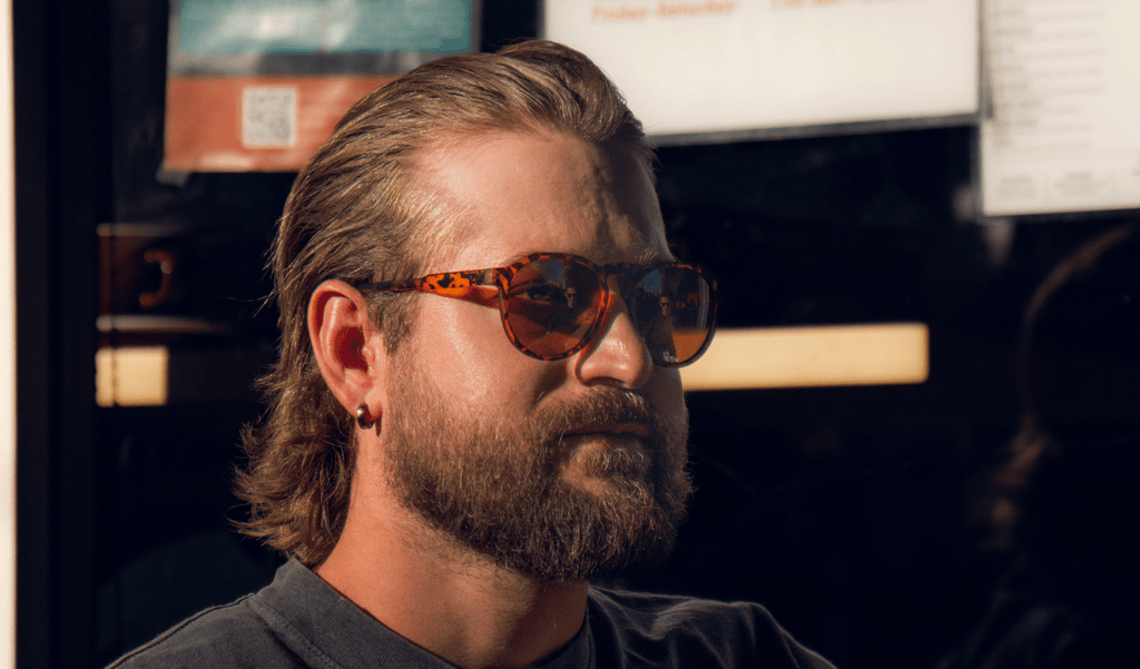 Man wearing Optic Nerve RiNO sunglasses with a tortoise frame and brown lens with a blurred background