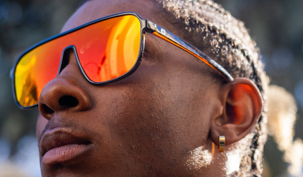 Close up of a man wearing Optic Nerve Montrose sunglasses with tortoise frame, smoke lens, and a red mirror on a blurred natural background