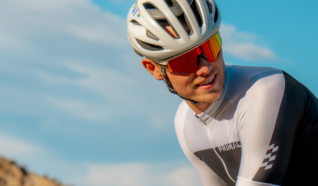 Cyclist wearing a helmet and Optic Nerve FixieAIR sunglasses with a white frame, smoke lens, and red mirror, with a clear blue sky in the background