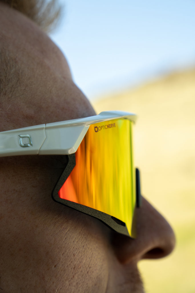 Close-up of a person wearing FixieAIR sunglasses with a white frame, smoke lens, and red mirror, with a blurred background