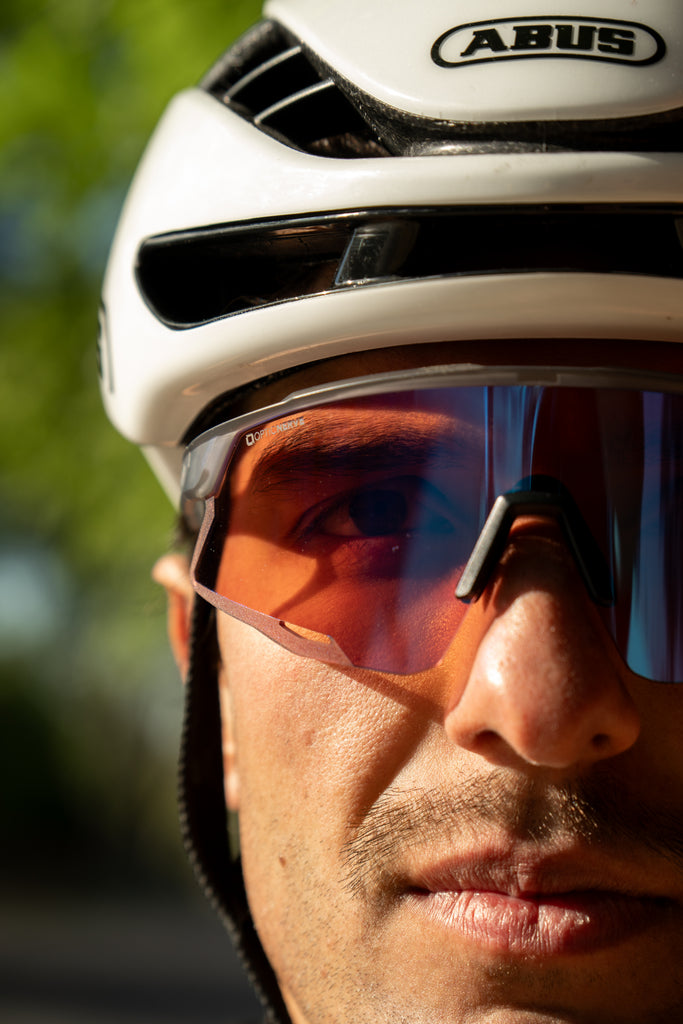 Close up of a cyclist wearing FixieAIR sunglasses with a gray frame, smoke lens, and red mirror on a blurred background