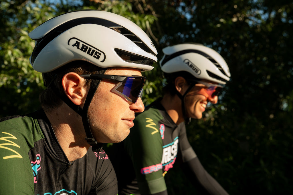 Two cyclists wearing ABUS helmets and Optic Nerve FixieAIR sunglasses with a blurred natural background