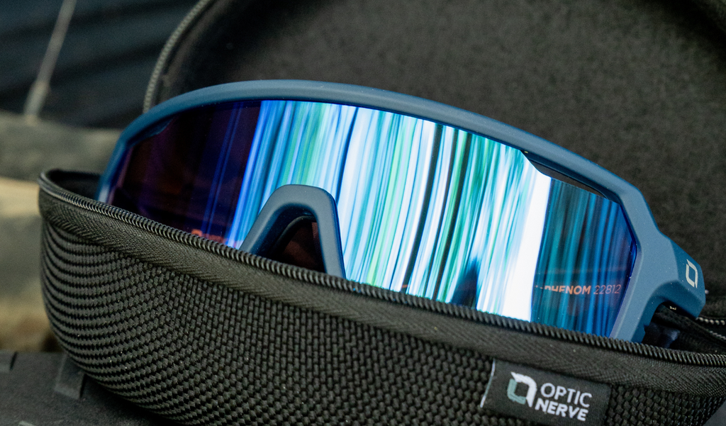 Close up of Optic Nerve FixiePHENOM 2.0 sunglasses with a blue frame, copper lens, and a silver mirror in an Optic Nerve hard case