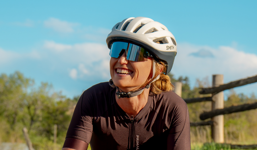 Cyclist with a white helmet and FixieSLICE sunglasses with a blue frame, smoke lens, and a silver mirror with a natural background