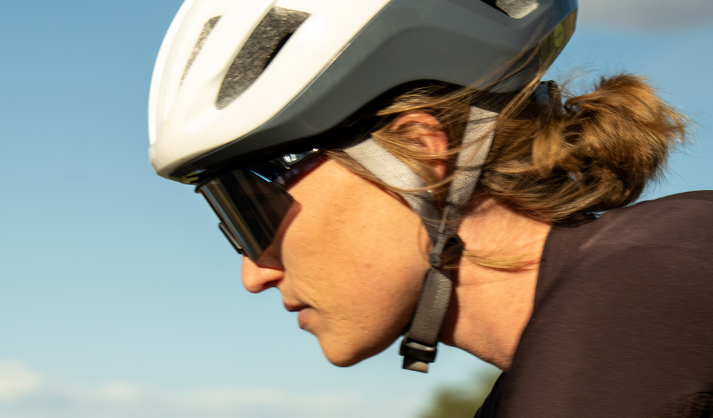 Close up portrait of a cyclist wearing a white helmet and FixieSLICE sunglasses with a blue frame, smoke lens, and a silver mirror