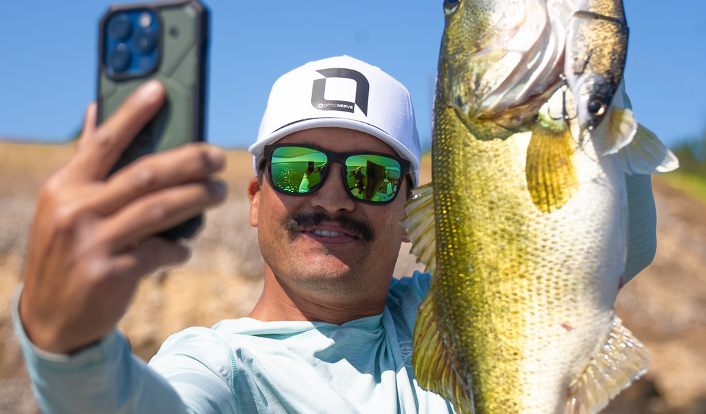 Chris Zaldain taking a selfie of a fish he caught wearing an Optic Nerve cap and Optic Nerve Zaldaingerous FixieMAX sunglasses with a tortoise frame, amber lens, and a green mirror