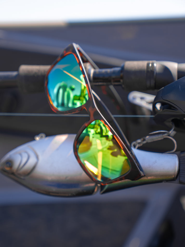 Close up of Zaldaingerous Rumble sunglasses with a tortoise frame, high-def color tuned amber lens, and a green mirror hanging from a fishing pole