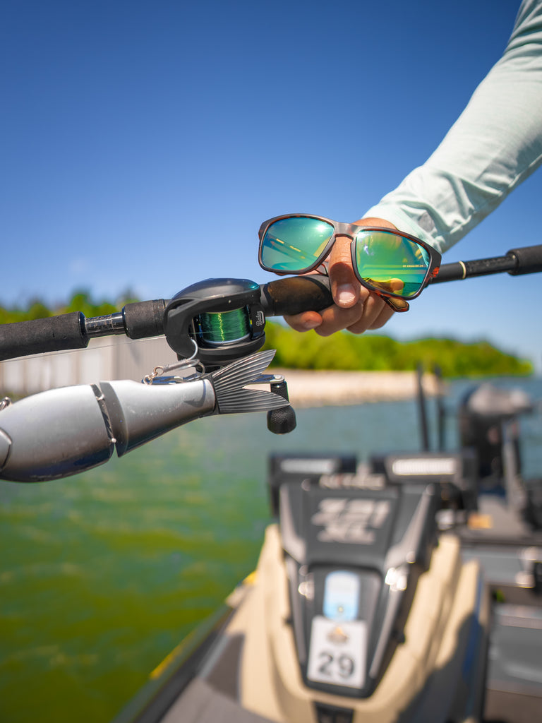 Close up of Zaldaingerous Rumble sunglasses with a tortoise frame, high-def color tuned amber lens, and a green mirror on a fishing pole with a blurred background