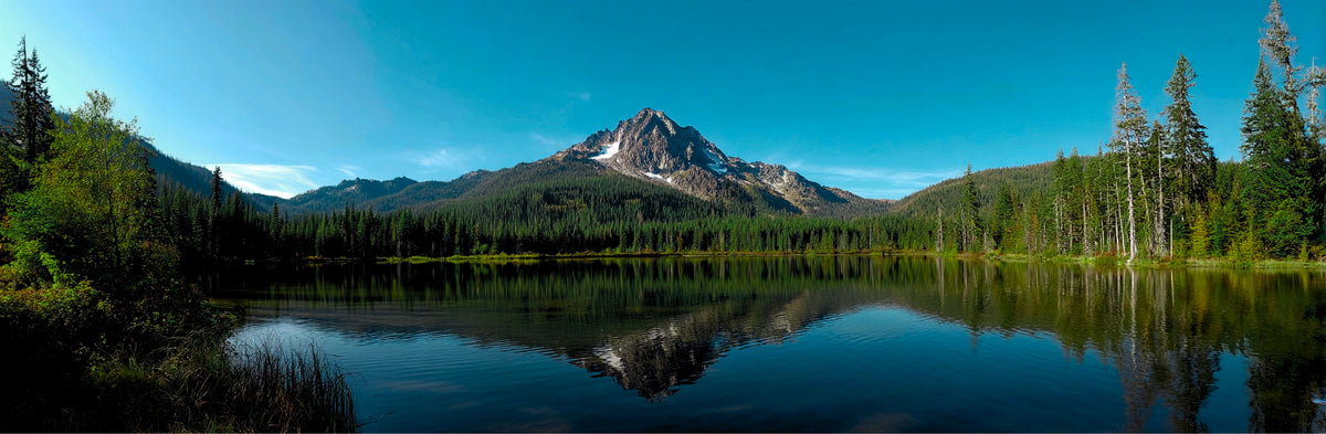 Panoramic view of a mountain reflected in a calm lake with trees around.