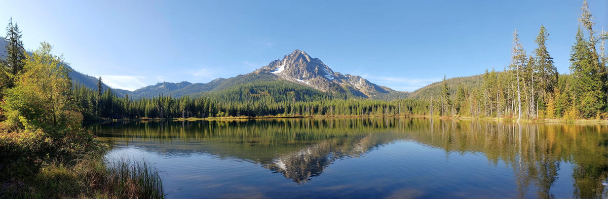 Panoramic view of a mountain reflected in a calm lake with trees around.
