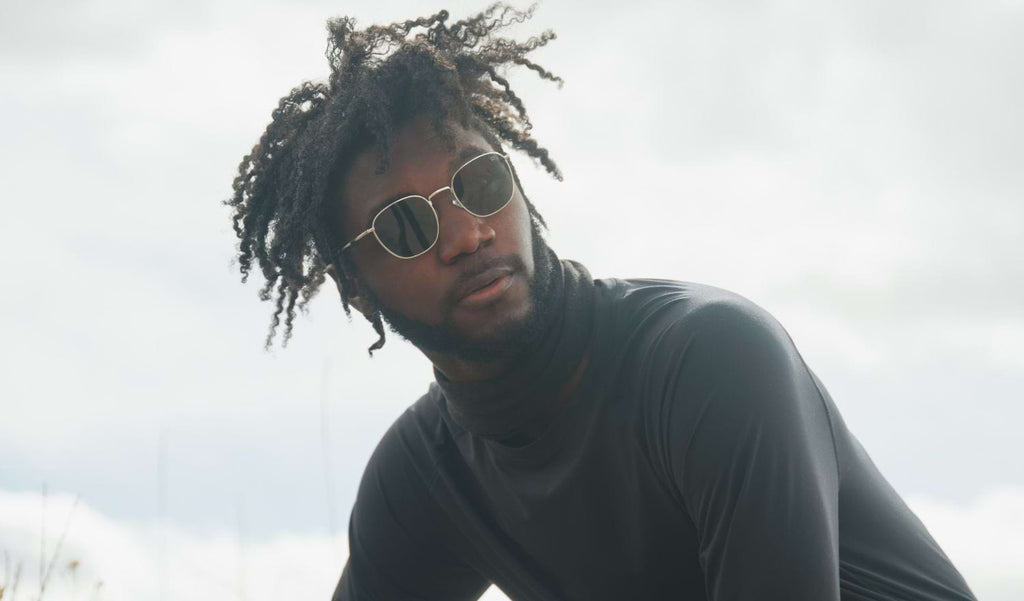 Man wearing Optic Nerve Townsend sunglasses with a gold frame and smoke lenses, with a gray sky background