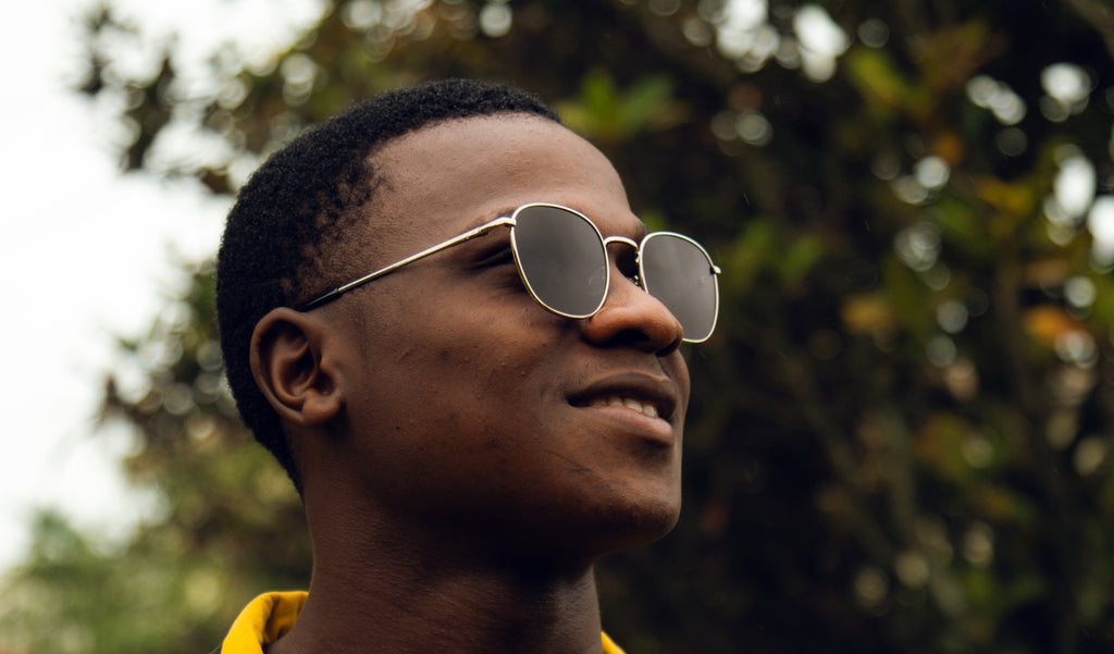Close up of a man wearing Optic Nerve Townsend sunglasses with a silver frame and smoke lenses with a blurred natural background.