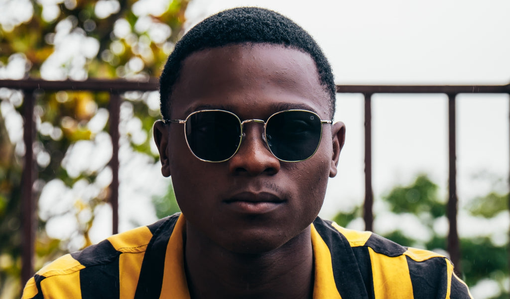 Close up of a man wearing Optic Nerve Townsend sunglasses with a silver frame and smoke lenses with a blurred background.