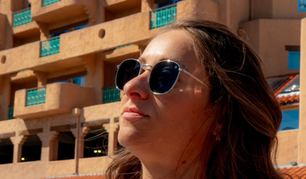 Woman wearing Optic Nerve Townsend sunglasses with a silver frame and smoke lenses, with a modern architectural building in the background