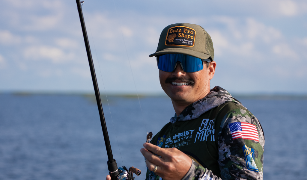 Man fishing on a boat wearing a cap and Optic Nerve Zaldaingerous FixieMAX sunglasses with a black frame, amber lens, and blue mirror, with a blurred background