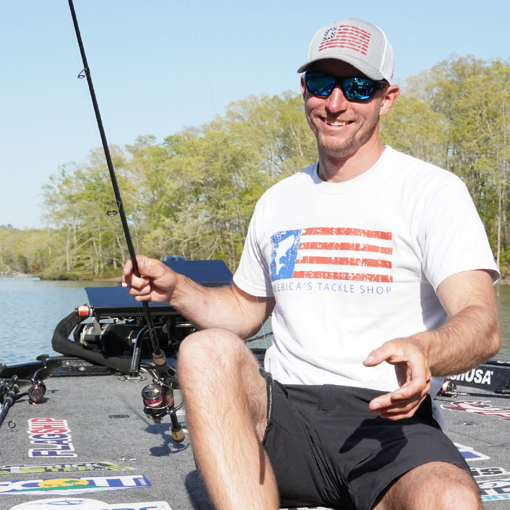 Man sitting on a boat holding a fishing rod wearing Optic Nerve sunglasses with a scenic background