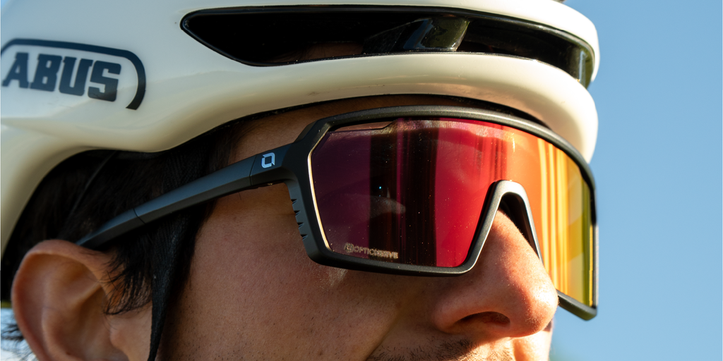 Close up of a man wearing a white helmet and Optic Nerve FixiePHENOM 2.0 Photochromic sunglasses with a black frame, photochromic lens, and a red mirror.