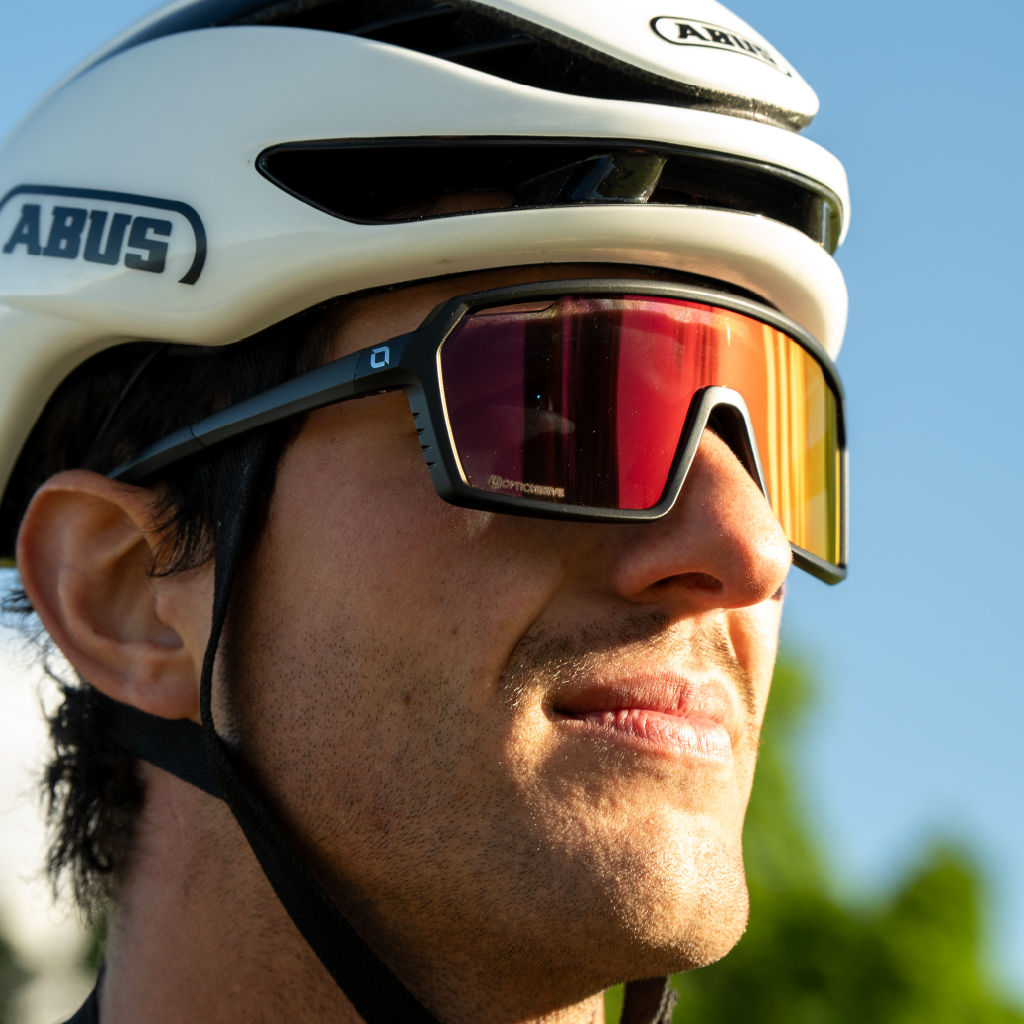 Close up of a man wearing a white helmet and Optic Nerve FixiePHENOM 2.0 Photochromic sunglasses with a black frame, photochromic lens, and a red mirror.