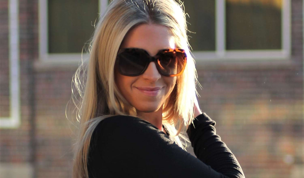 Woman wearing Optic Nerve Asana sunglasses with tortoise frame and brown lenses with a building in the background