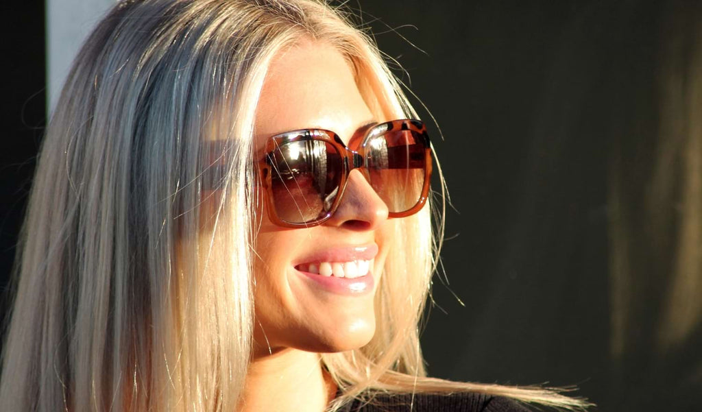 Woman wearing Optic Nerve Asana sunglasses with a tortoise frame and brown lenses against a blurred background