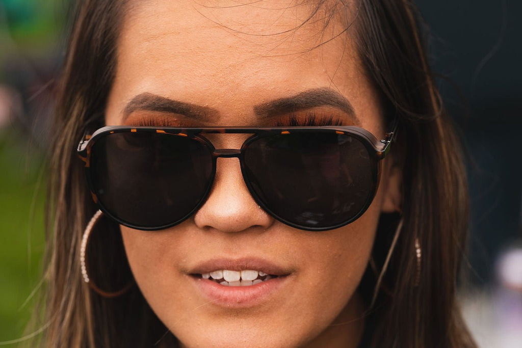 Close up of  a woman wearing Optic Nerve Govnah sunglasses with a tortoise frame and smoke lenses with a blurred background