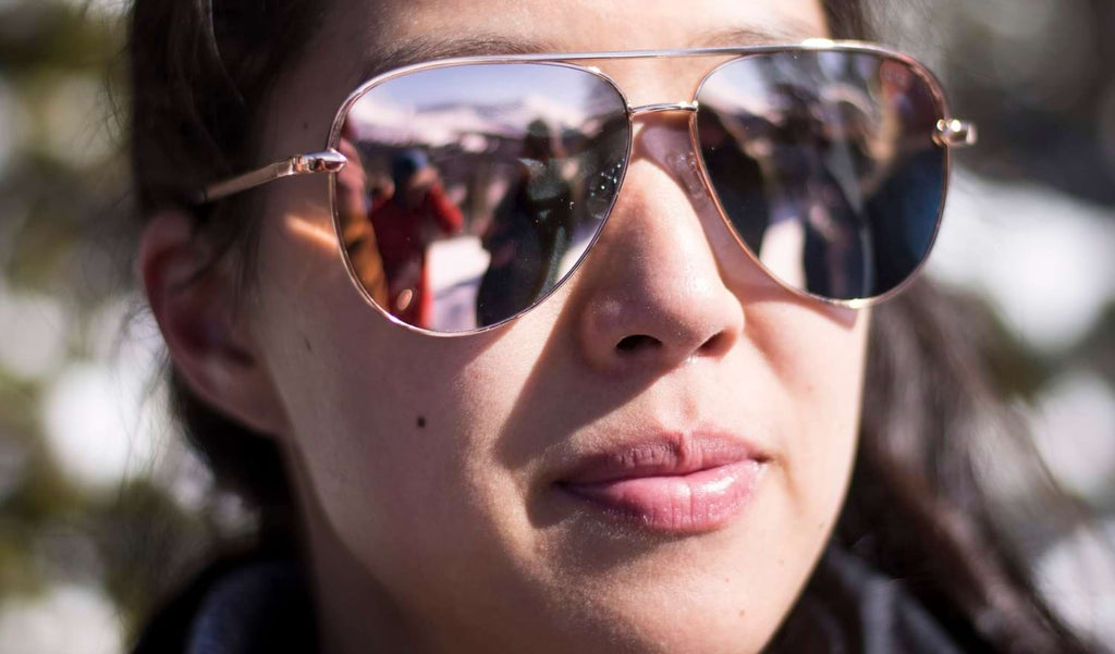 Close up of a woman wearing Optic Nerve Flatscreen sunglasses with rose gold frame, smoke lenses, and rose gold mirror